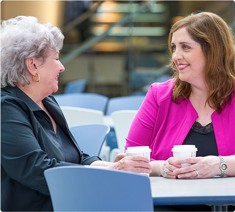 Two women sitting at a table in a hospital cafeteria drinking coffee and talking